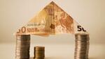 Una casa realizada con dos montones de monedas usados de pilares y un tejado de un billete de 50 euros