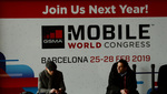 Dos personas están sentadas con un cartel detrás de la Mobile World Congress